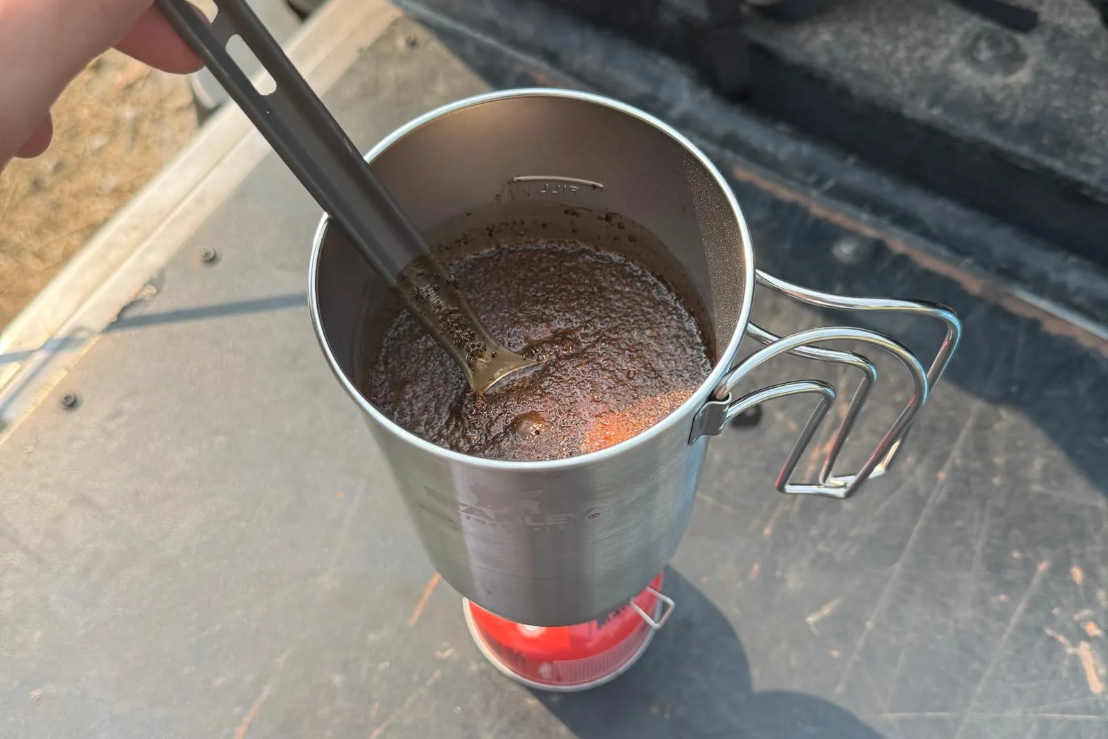 Coffee steeping in the Stanley pot on the stove, stirred with a spork